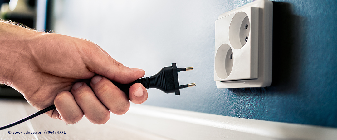 Eine Hand hält einen  Stromstecker nahe einer Steckdose Eine Hand hält einen  Stromstecker nahe einer Steckdose
